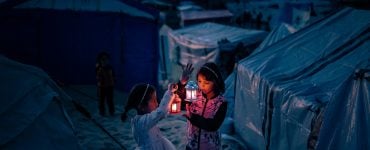 Two young girls in a refugee camp hold glowing lanterns against the backdrop of tents, their faces illuminated with warmth and resilience amidst the darkness. This image reflects the spirit of Gaza in Ramadan—caught between hardship and hope, echoing the soul’s journey between Pharaoh’s oppression and the Divine promise